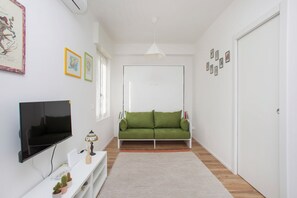 Ein modernes Wohnzimmer mit Flachbildfernseher, grünem Sofa, weißen Wänden und einer Tür.