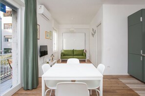 A modern interior with a white dining table, green sofa, and a TV on the wall.