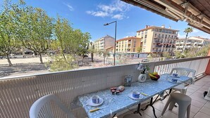 Un balcó amb una taula preparada per a dues persones, caires i una vista del carrer, amb edificis al fons.