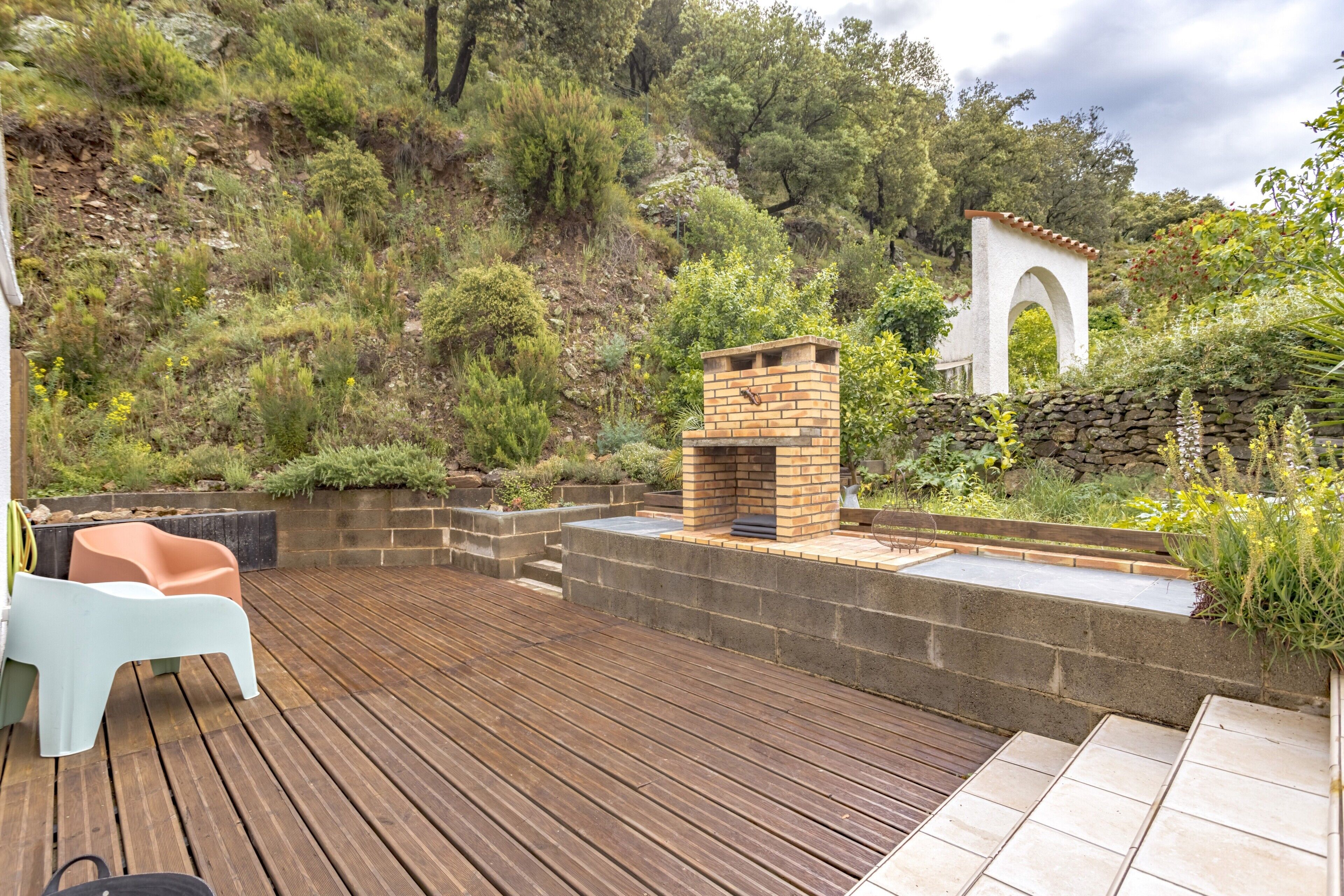Una terraza de madera con asientos incorporados, una chimenea de ladrillo y un muro de contención de piedra.