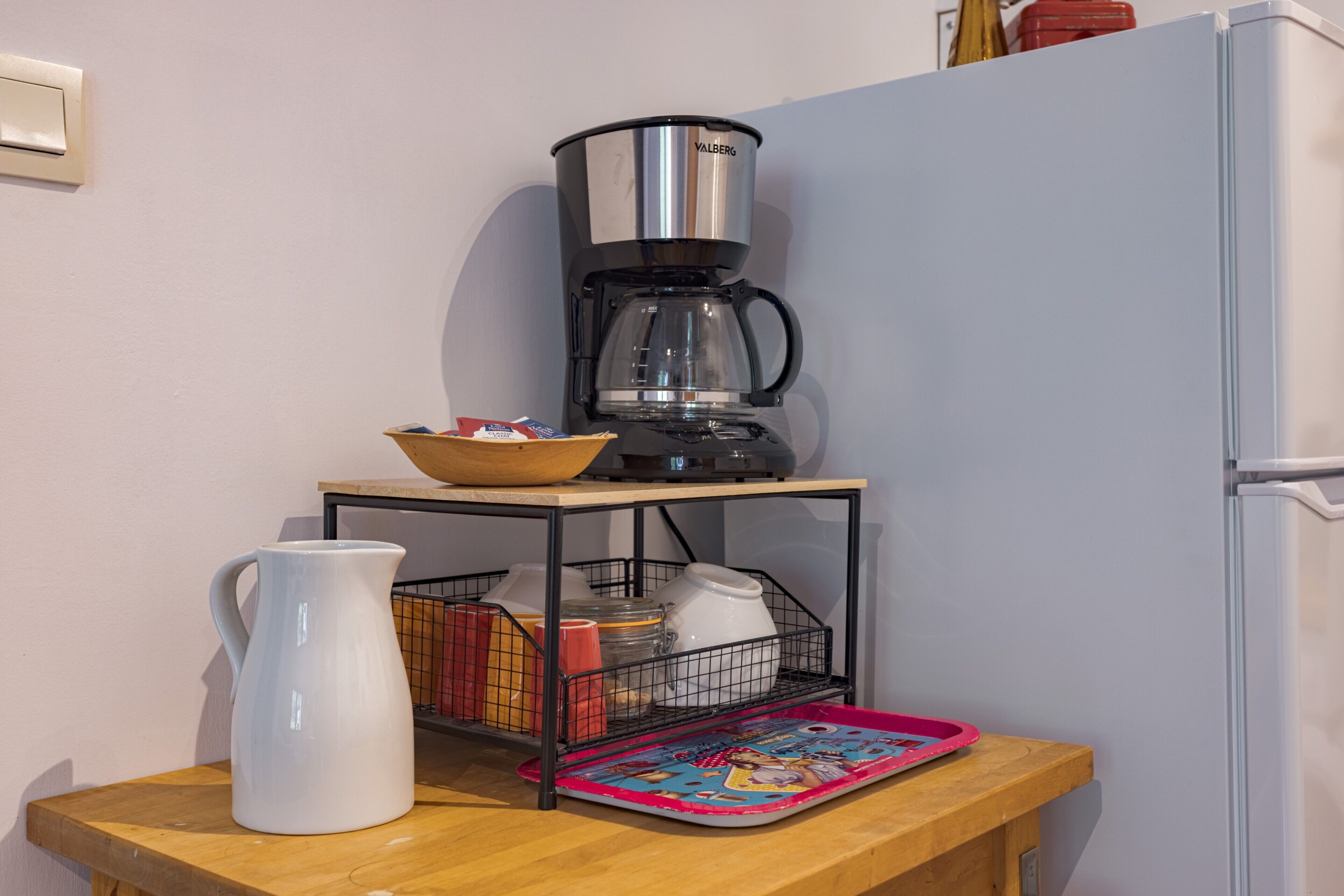 Una cocina con cafetera, jarra, bandeja y refrigerador.