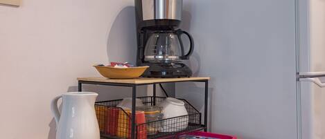 Una cocina con cafetera, jarra, bandeja y refrigerador.