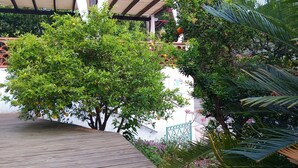 Une terrasse en bois, un mur blanc agrémenté d’une grille en métal décorative et un feuillage verdoyant luxuriant.