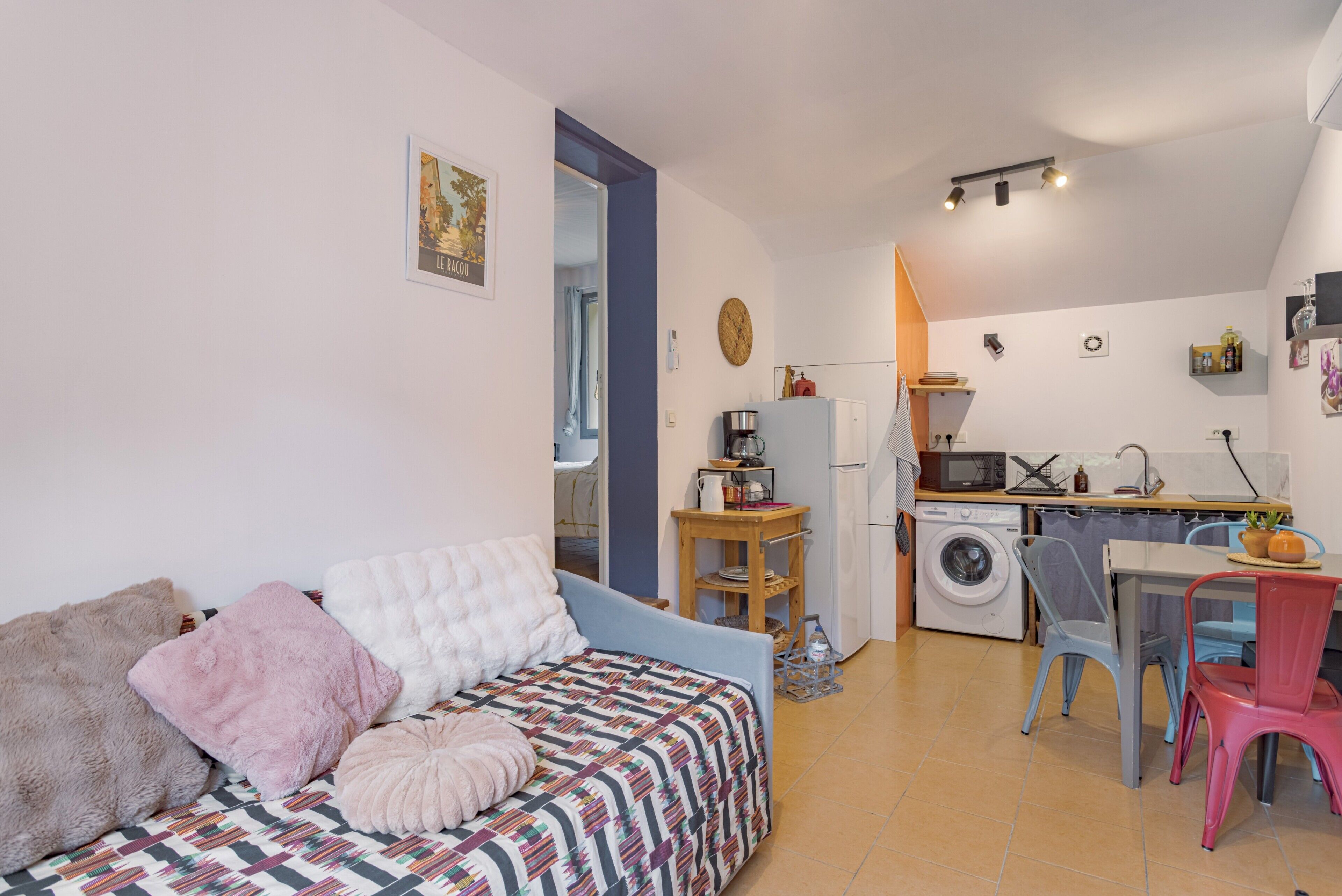 Un espacio habitable compacto con sofá, una pequeña cocina que incluye lavadora y una mesa de comedor con sillas.