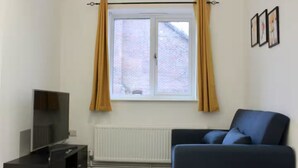 Una habitación con ventana, radiador, televisión y una silla azul.