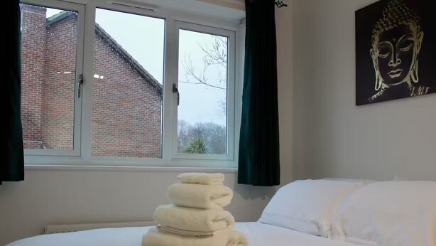 Una cama con sábanas blancas, una ventana con vista a un edificio de ladrillo y un cuadro de Buda en la pared.