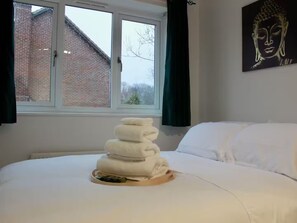 A bed with white linens, a window with a view of a brick building, and a Buddha painting on the wall.