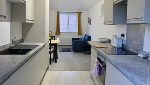 Una cocina compacta con un lavamanos, un comedor con una mesa y sillas, un sofá azul y una ventana con cortinas.