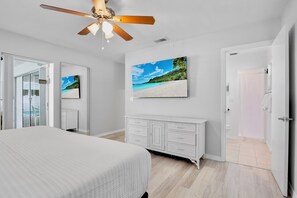 A bedroom with a bed, a ceiling fan, a white dresser, and a beach scene painting on the wall. - Mermaid Dreams - Perfect Location Close to Everything! (Bradenton)