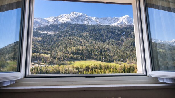 Une fenêtre donnant sur un paysage montagneux, avec des pics enneigés et une forêt dense.