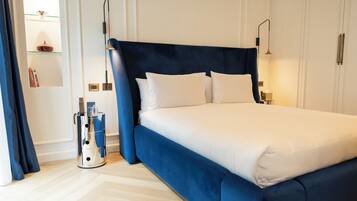 A neatly made bed with a dark headboard, a bedside table with a lamp, and a small shelf with books and decorative items.