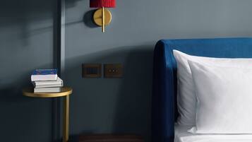 Una camera da letto con un letto, un comodino, un poggiapiedi rosso e una lampada a parete.