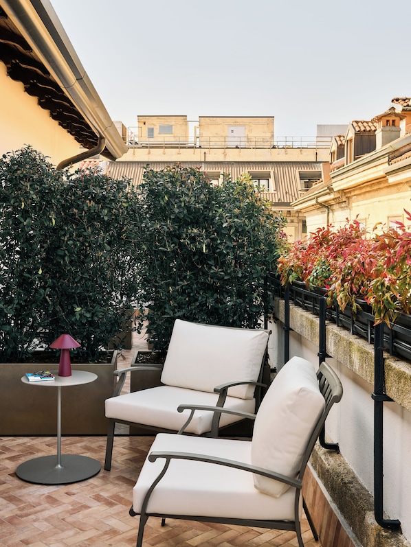 An outdoor seating area with two white cushioned chairs, a small round table with a lamp, and a potted plant. - Casa Laveni (Milan)