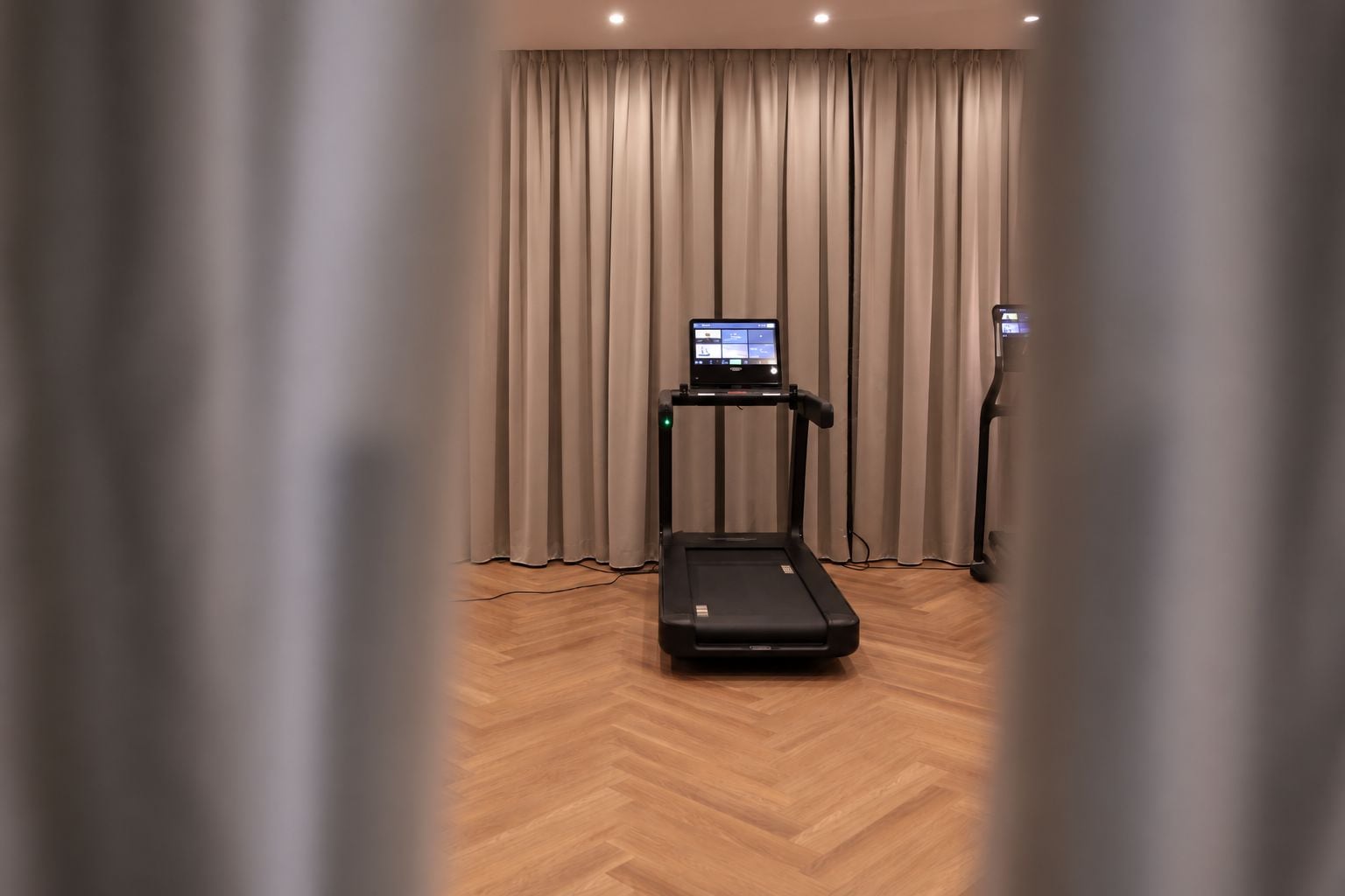 Een kamer met een loopband, een digitaal scherm en een hometrainer.
