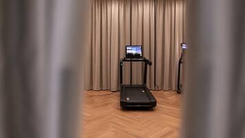 A room with a treadmill, a digital display, and a standing exercise bike.