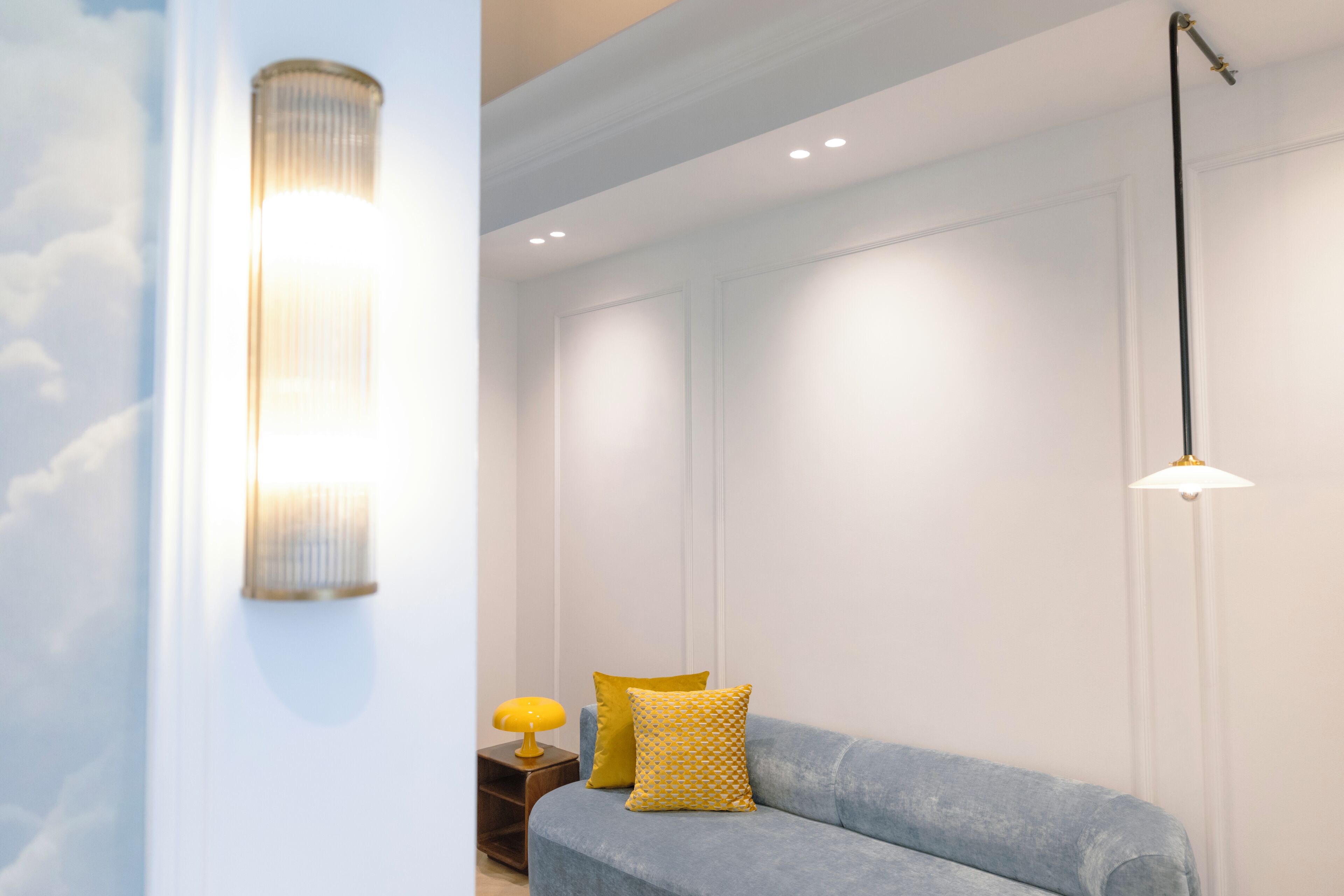 A room with a blue sofa, a yellow lamp, and a wall-mounted light fixture.