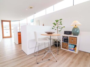 A modern kitchen with white cabinetry, a wooden dining table, and a potted plant. - 12 Nautilus (Bideford)