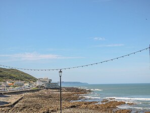 A coastal area with a rocky shoreline, buildings along the coast, and a clear sky. - 12 Nautilus (Bideford)