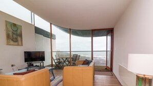 A modern living room with a television, two sofas, a dining table, and a balcony with a view. - 12 Nautilus (Bideford)