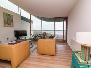 A modern living room with a television, two sofas, a dining table, and a balcony with a view. - 12 Nautilus (Bideford)