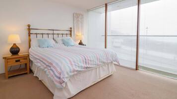 A bedroom with a bed, nightstands, a lamp, and a large window with blinds.