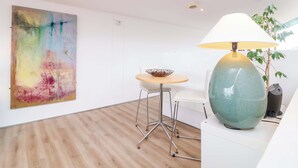 A modern room with a wooden floor, a round table with a bowl, a white chair, a large abstract painting, and a green lamp. - 12 Nautilus (Bideford)