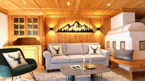 A cozy room with a wooden ceiling, a sofa with deer-themed pillows, a rocking chair, and a table with candles. - KitzSpirit by Belle-Stay (Kitzbühel)