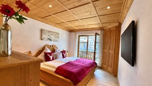 A bedroom with a wooden ceiling, a bed with a red blanket, a wooden dresser, a vase with flowers, and a painting on the wall. - KitzSpirit by Belle-Stay (Kitzbühel)