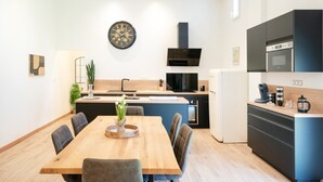 A modern kitchen with a wooden dining table, chairs, a clock, and built-in appliances.