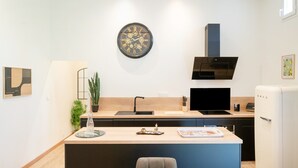 A modern kitchen with a central island, a wall-mounted clock, a built-in stove, and a white refrigerator.