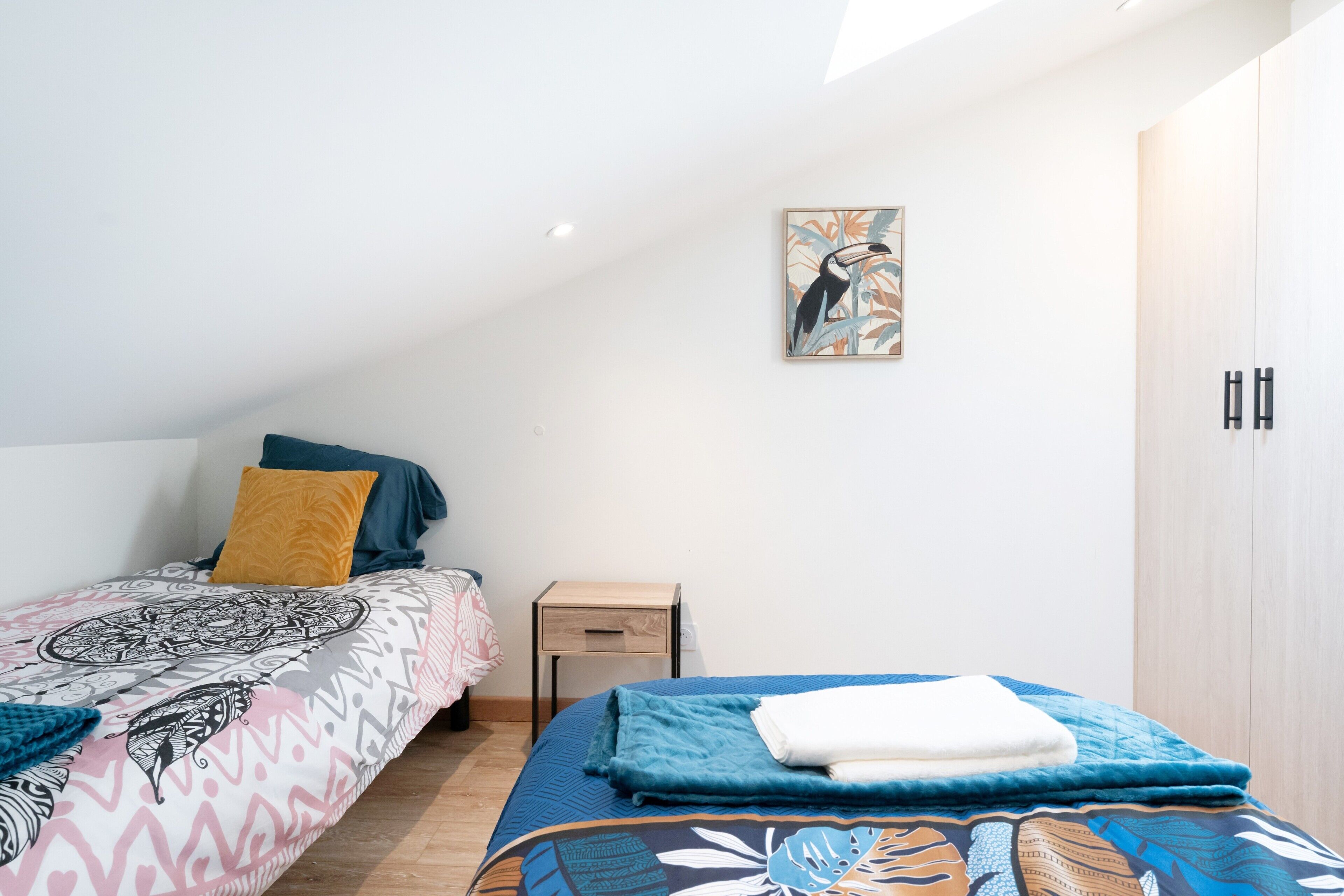 A bedroom with two beds, a small bedside table, a wardrobe, and a wall-mounted artwork.