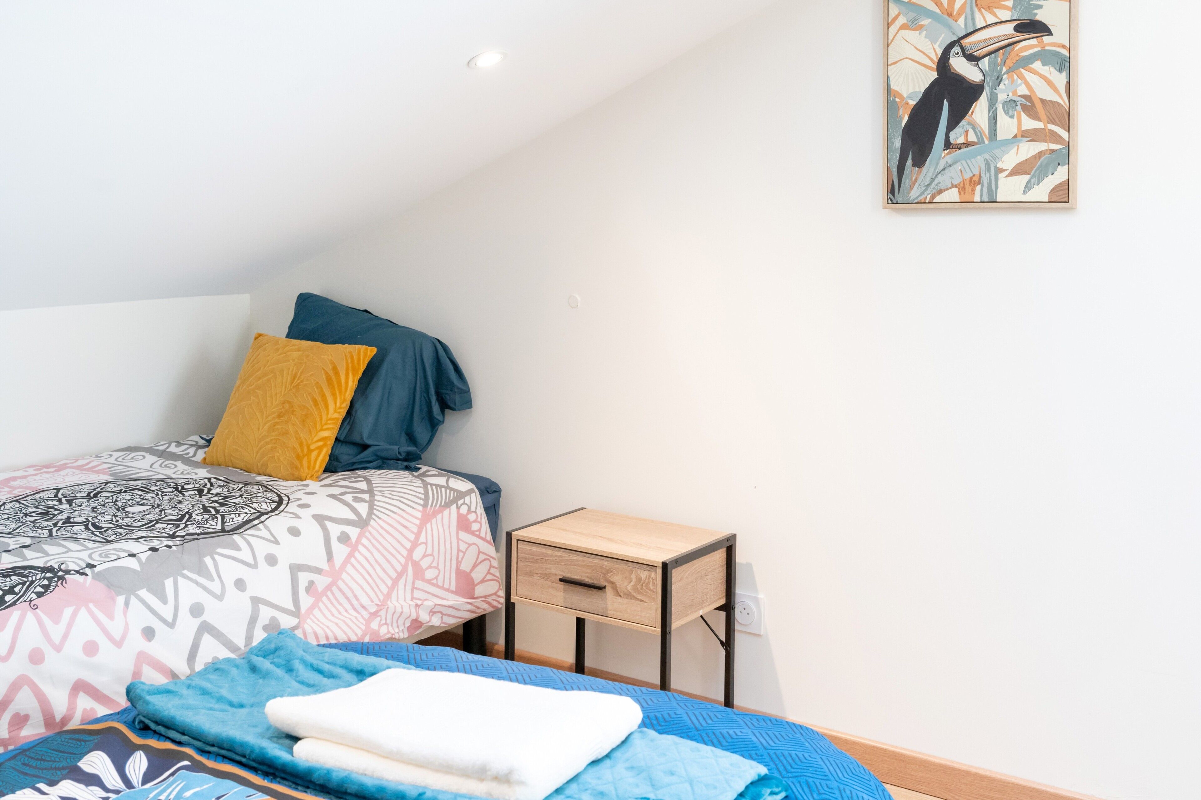 A bedroom with a bed, a nightstand, a wall-mounted artwork, and a ceiling light.