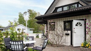 A white building with a black roof, a white door, and a small garden with a table and chairs. - Mellebyrundan by Interhome (Mellbystrand)