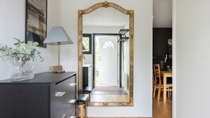 A hallway with a large ornate mirror, a desk with drawers, a lamp, and a vase with green plants. - Mellebyrundan by Interhome (Mellbystrand)