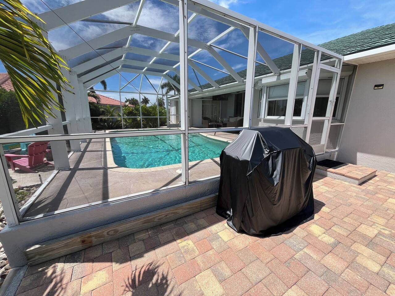 Un espace extérieur abrité comprenant une piscine, un barbecue couvert et une structure en verre.