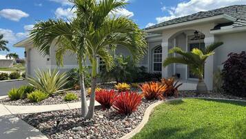 A residential property with a well-maintained lawn, a variety of colorful plants, and a white house with a tiled roof.