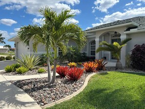 A residential property with a well-maintained lawn, a variety of colorful plants, and a white house with a tiled roof. - Salted Sunset at Punta Gorda Isles (Punta Gorda)