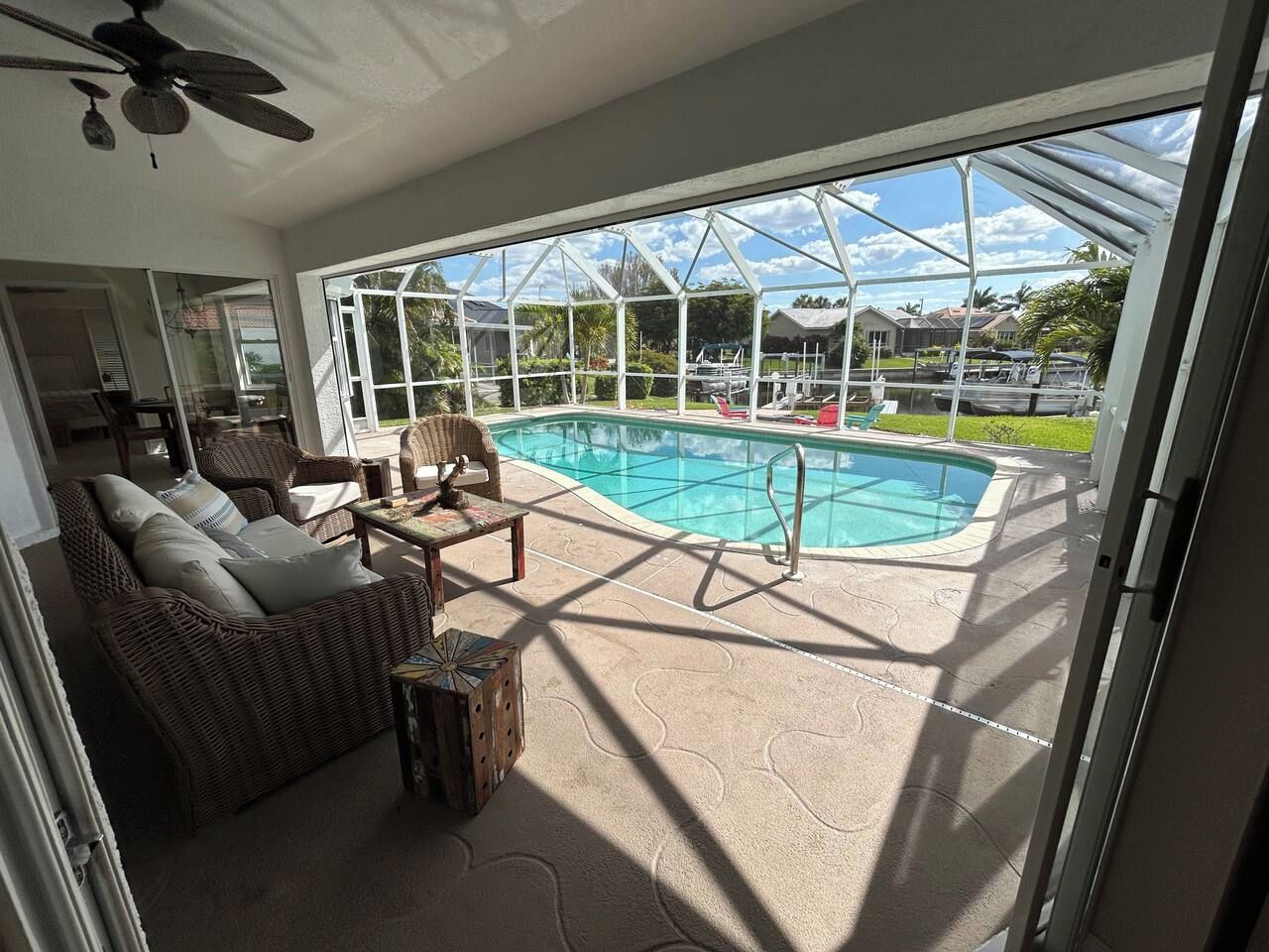 Ein überdachter Außenbereich mit Pool, Korbmöbeln und Deckenventilator.