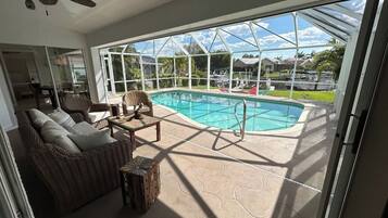 Ein überdachter Außenbereich mit Pool, Korbmöbeln und Deckenventilator.