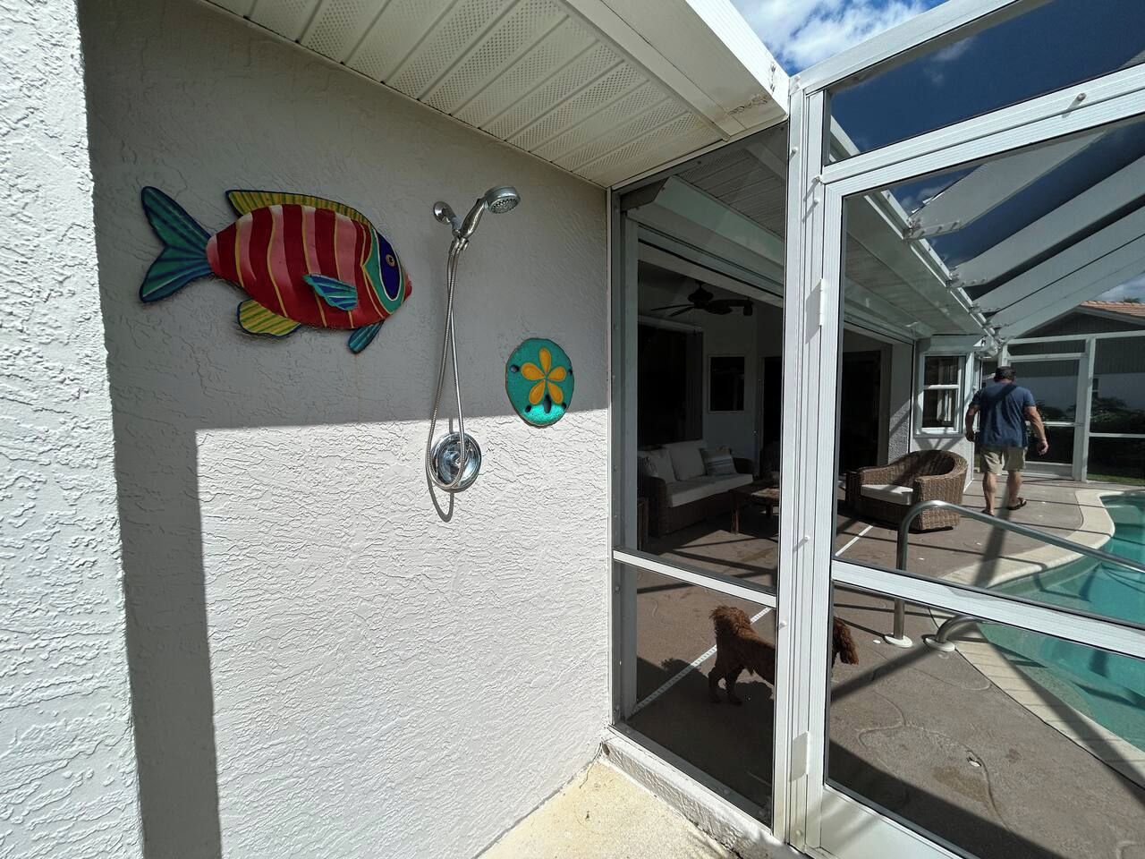 A poolside area with a glass door, a shower, and a dog.