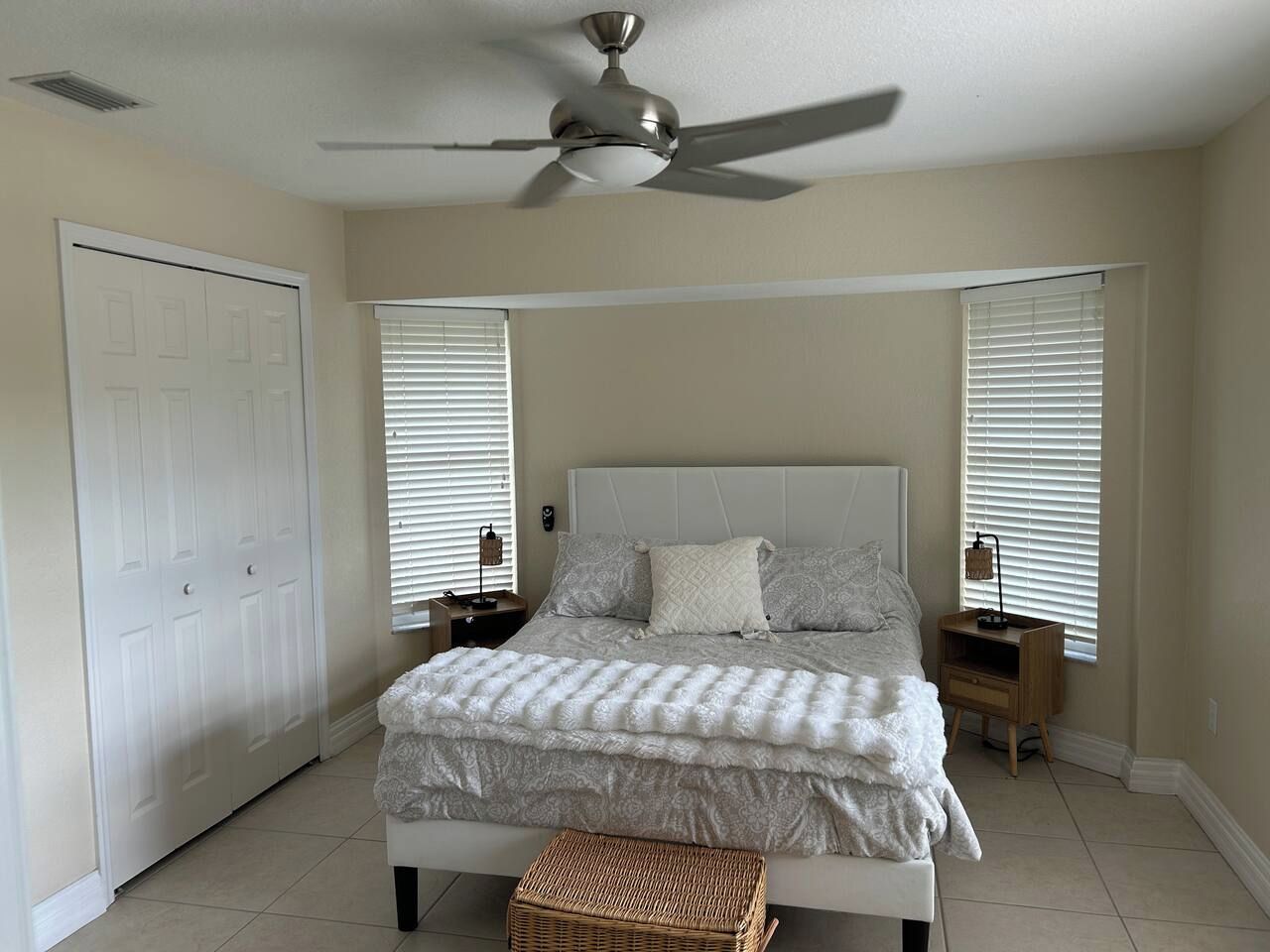 A bedroom with a bed, a ceiling fan, a nightstand, and a window with blinds.