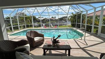 A covered outdoor area with a pool, wicker furniture, and a view of a residential neighborhood.