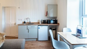 Une cuisine compacte équipée d’un évier, d’un four à micro-ondes et d’un petit réfrigérateur. Un coin repas avec une table et des chaises est également disponible.