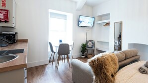 Une chambre d’hôtel moderne dotée d’un coin cuisine, d’une table à manger avec des chaises, d’un grand téléviseur à écran plat fixé au mur, d’un canapé agrémenté d’un plaid moelleux et d’un miroir.