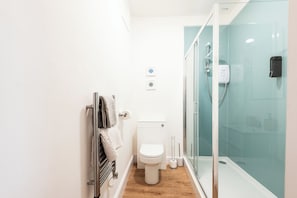 Un baño con inodoro, toallero, cabina de ducha de vidrio y un lavamanos pequeño.