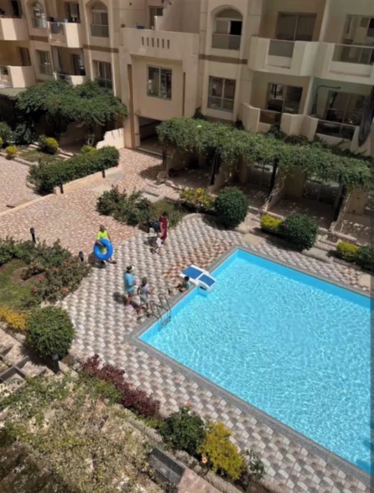 Una piscina rodeada por un patio con suelo de baldosas y vegetación.