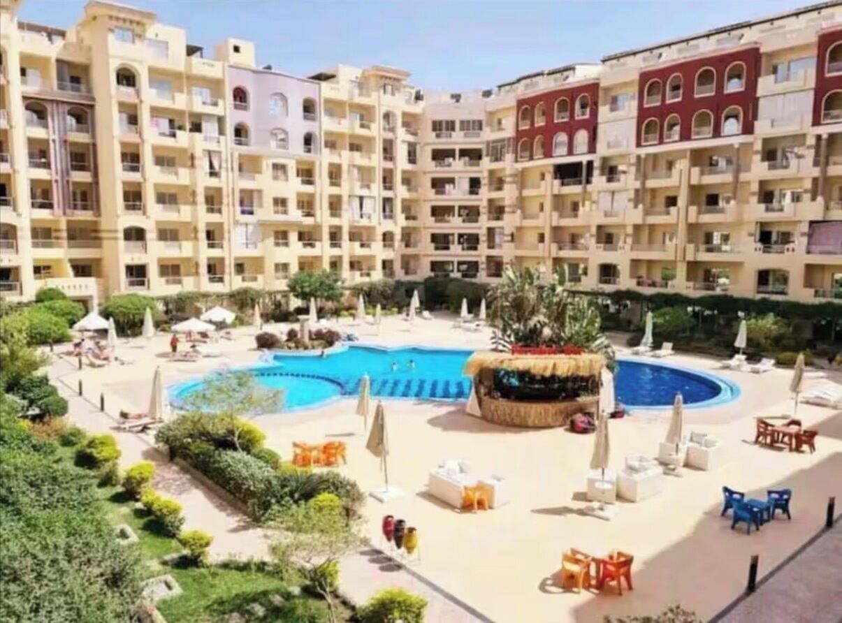 A multi-story hotel with a central swimming pool surrounded by lounge chairs and umbrellas.
