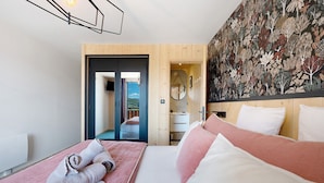 A hotel room with a bed, a wooden door, a mirror, and a wall with a leaf pattern.