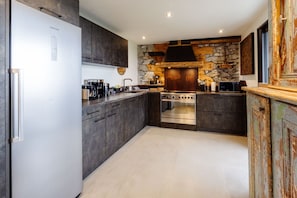 Une cuisine moderne dotée d’une cuisinière intégrée, d’un réfrigérateur et de meubles de rangement aux couleurs sombres.