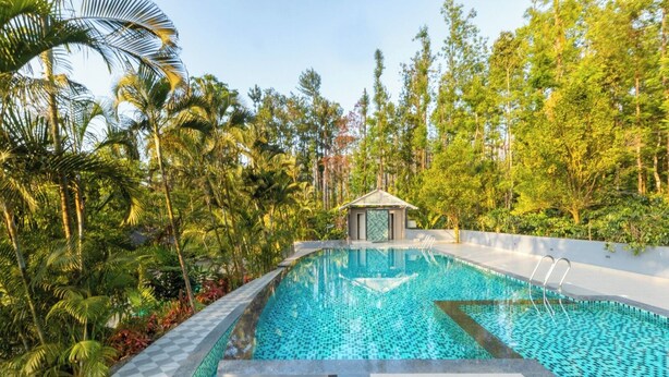 A swimming pool with a checkered border, surrounded by lush greenery and a small pavilion. - KAVA RETREAT (Chikkamagaluru)